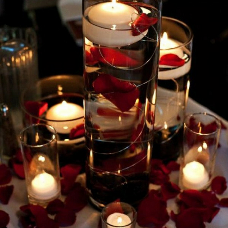 Bulk romance red rose petals for romantic wedding décor – Prime Petal Company. Decorative candles with red rose petals in glass containers on a table.