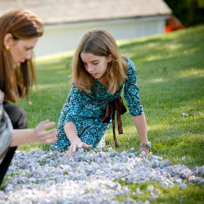 Bulk wine green hydrangea petals for wedding and event décor – Prime Petal Company. Woman and young girl placing blue hydrangea petals on a grass wedding aisle
