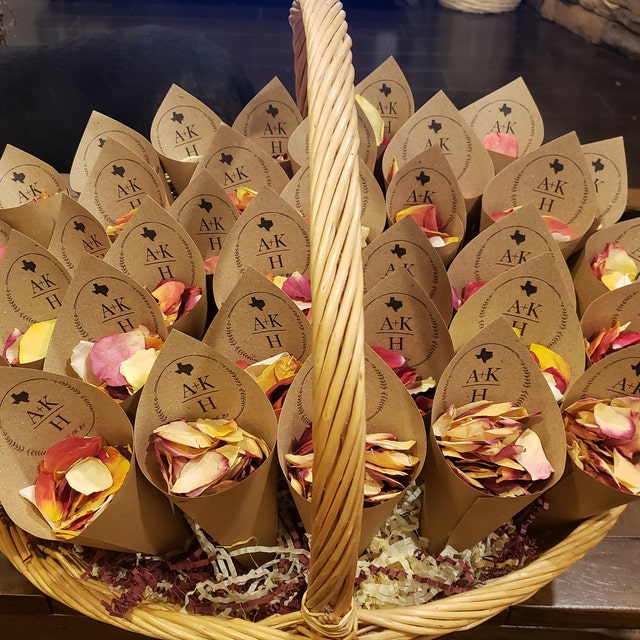 Bulk Sunset Serenade warm-toned rose petals for outdoor weddings – Prime Petal CompanyBasket filled with paper cones containing flower petals and branded labels. 