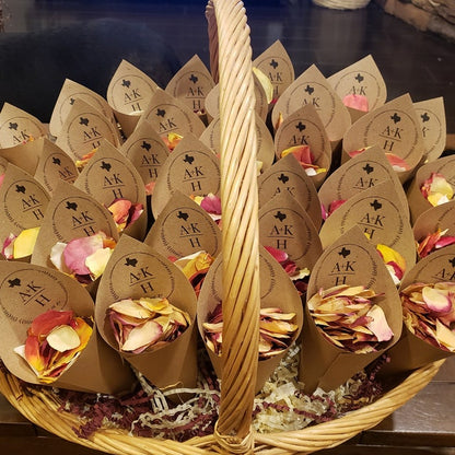 Bulk Sunset Serenade warm-toned rose petals for outdoor weddings – Prime Petal CompanyBasket filled with paper cones containing flower petals and branded labels. 