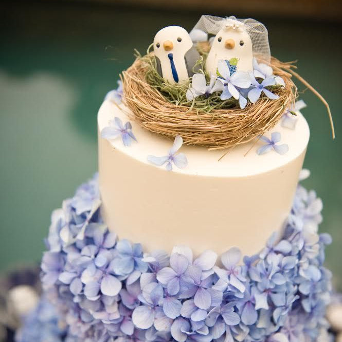 Bulk blue green hydrangea petals for wedding décor – Prime Petal Company. Two-tiered wedding cake with blue hydrangeas and bird figurines on top