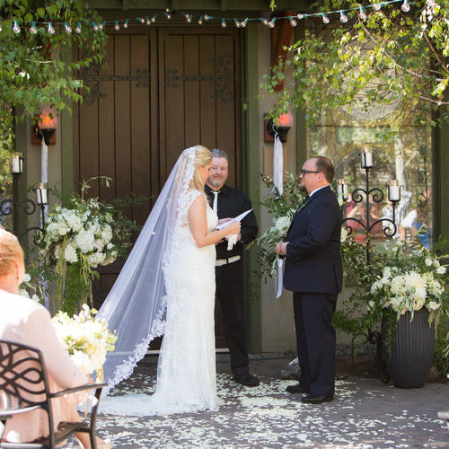 Bulk ivory rose petals for elegant wedding aisle and event décor – Prime Petal Company. Outdoor wedding ceremony with the bride and groom at the altar surrounded by ivory rose petals