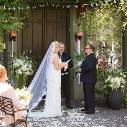 Bulk ivory rose petals for elegant wedding aisle and event décor – Prime Petal Company. Outdoor wedding ceremony with the bride and groom at the altar surrounded by ivory rose petals