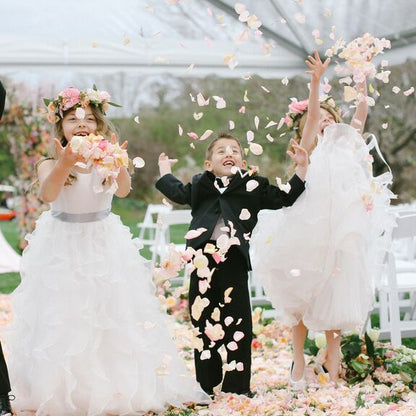 Bulk ivory cream blush rose petals for soft-toned wedding décor – Prime Petal Company. Children in formal attire are throwing flower petals at a wedding ceremony.