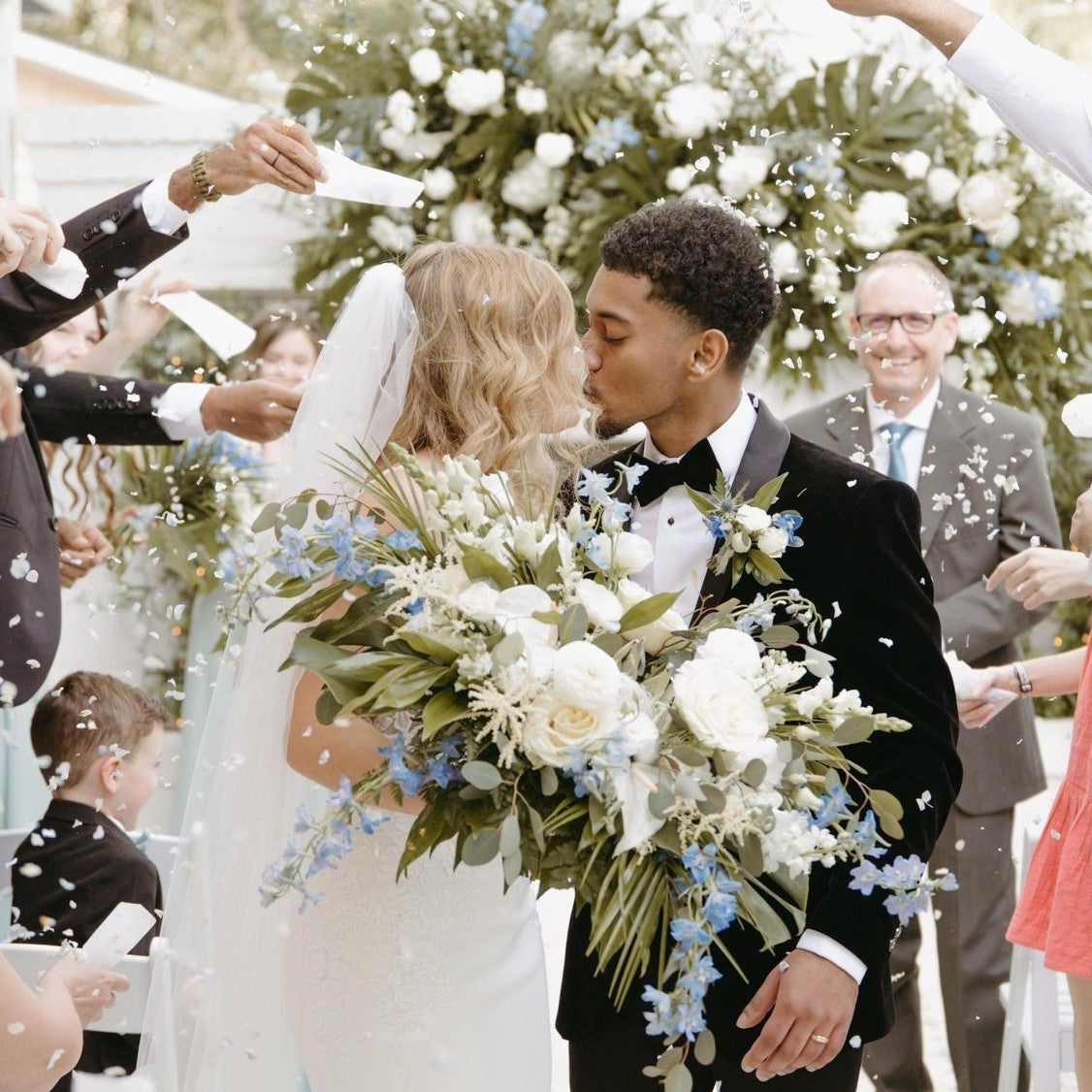 Wedding scene with bride and groom surrounded by guests throwing biodegradable petal confetti.