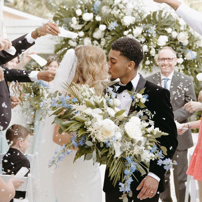 Wedding scene with bride and groom surrounded by guests throwing biodegradable petal confetti.