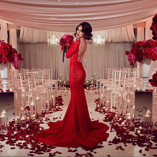 Bulk crimson rose petals for rich red wedding and event décor – Prime Petal Company. Woman in a red evening gown holding flowers in a decorated indoor setting with candles, rose petals and floral arrangements.