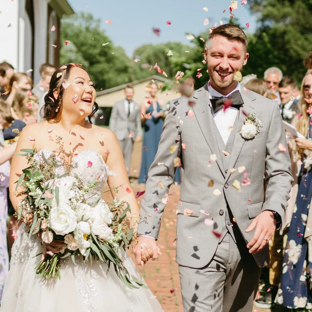Bulk Blissful Bloom mixed flower petals for weddings and events – Prime Petal Company. Wedding couple walking down the aisle with bidegradable confetti falling around them.