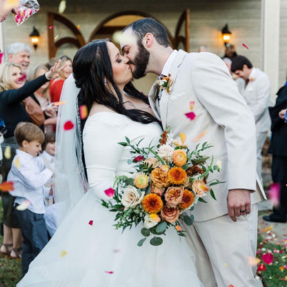 Couple kissing at a wedding with a colorful bouquet and confetti. Bulk Peppermint Twist rose and hydrangea petal blend for weddings – Prime Petal Company
