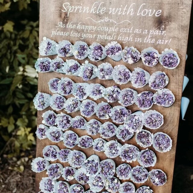 Decorative display of purple and lavender lilac petal tossing cones arranged on a wooden board with text.