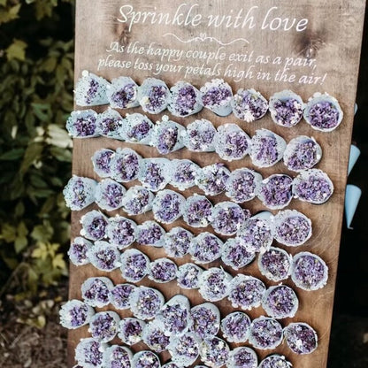 Decorative display of purple and lavender lilac petal tossing cones arranged on a wooden board with text.