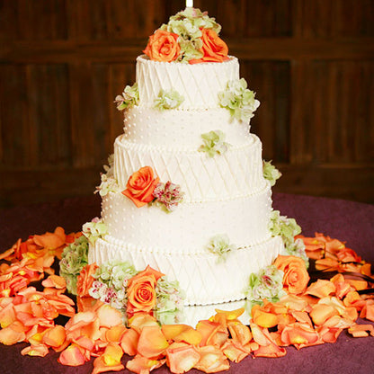Bulk orange ombre gradient rose petals for fall weddings – Prime Petal Company. Three-tiered wedding cake decorated with orange and green flowers and rose petals.