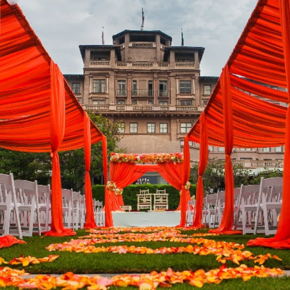 Bulk orange ombre gradient rose petals for fall weddings – Prime Petal Company. Decorative wedding setup with orange rose petals and fabric lining the wedding aisle.