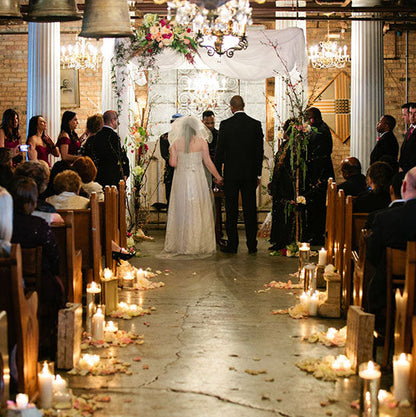 Bulk ivory rose petals for elegant wedding aisle and event décor – Prime Petal Company. Wedding ceremony in a rustic indoor setting with candles and floral arrangements.