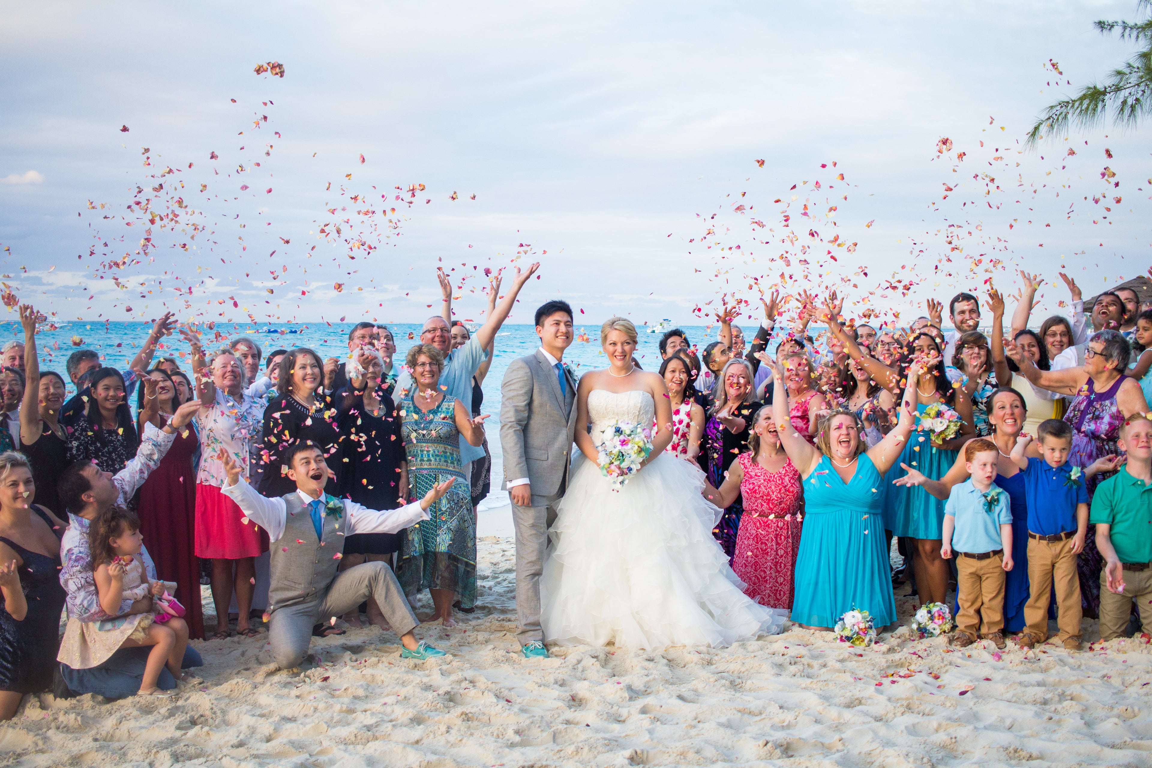Wedding couple with guests on a beach, tossing biodegradable petal confetti