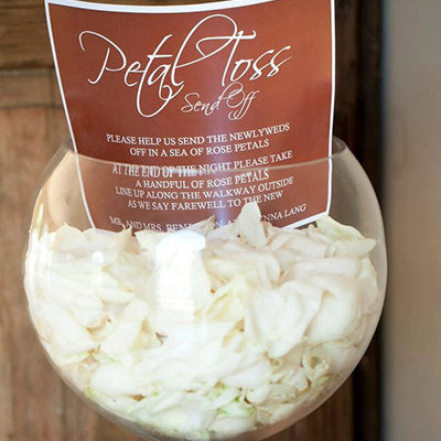 Bulk ivory rose petals for elegant wedding aisle and event décor – Prime Petal Company. Glass vase filled with ivory rose petals and a 'Petal Toss' sign 