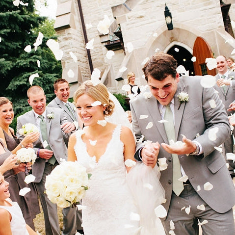 Bulk yellow rose petals for bright wedding aisle and party décor – Prime Petal Company. Wedding couple standing in front of a church with biodegradable rose confetti falling around them.