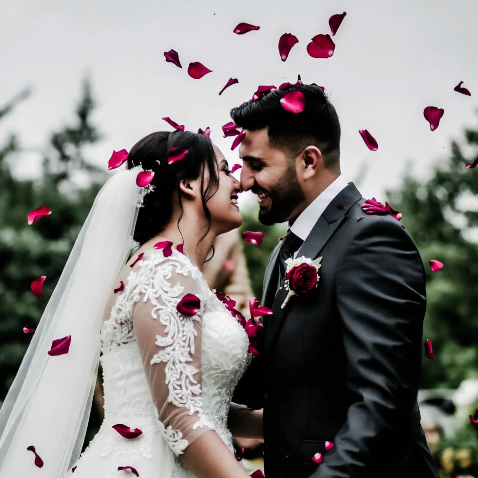Bulk ruby rose petals for weddings and romantic events – Prime Petal Company. wedding couple surrounded by red rose petals outdoors.