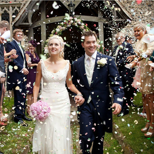 Bulk blue green hydrangea petals for wedding décor – Prime Petal Company. A Wedding couple walking through biodegradable confetti with guests on a grassy area. 